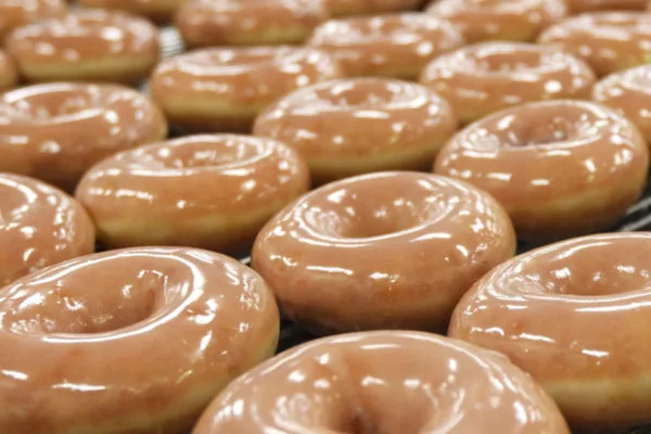 A close-up of several Krispy Kreme donuts, glimmering with a translucent glaze | Multiple Locations