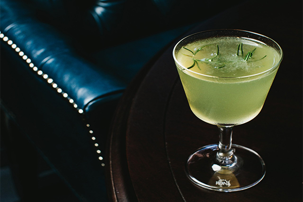 Green cocktail with a sprig of rosemary floating in it served atop a table in front of a black leather chair | 75 14th St NE, Atlanta, GA 30309