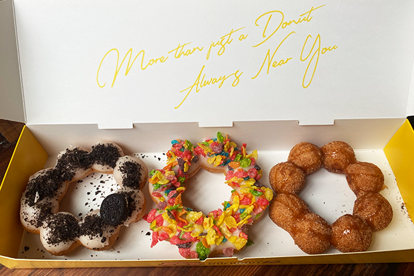 Three uniquely-shaped donuts in a yellow box, one topped with white glaze and black cookies crumbs, the next topped with rainbow cereal, and the third topped with a caramel glaze | 1235 Chattahoochee Ave NW, Atlanta, Georgia 30318